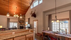 A spacious kitchen with a large island, stone wall, and a mounted deer head. - Wintergreen Chalet (Cle Elum)