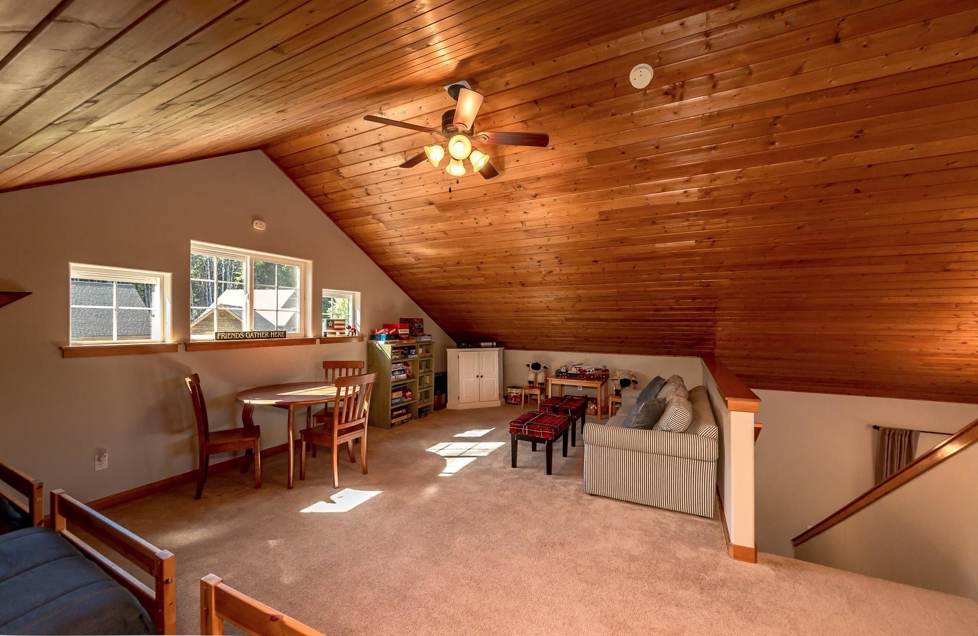 A cozy attic room with a sloped ceiling, wooden beams, a ceiling fan, and a dining area with a table and chairs.
