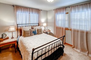 Un dormitorio con una cama, dos mesitas de noche, lámparas y cortinas.