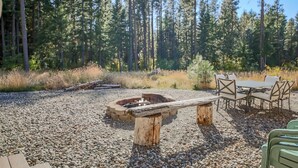 A rustic outdoor seating area with a fire pit, surrounded by a gravel ground and a forest backdrop. - Wintergreen Lodge (Cle Elum)