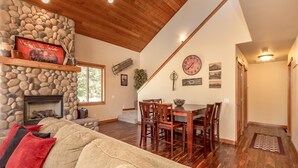 A cozy living room with a stone fireplace, wooden ceiling, and a dining area with a wooden table and chairs. - Wintergreen Lodge (Cle Elum)