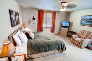 A bedroom with a bed, a TV, a dresser, a chair, and a painting on the wall.