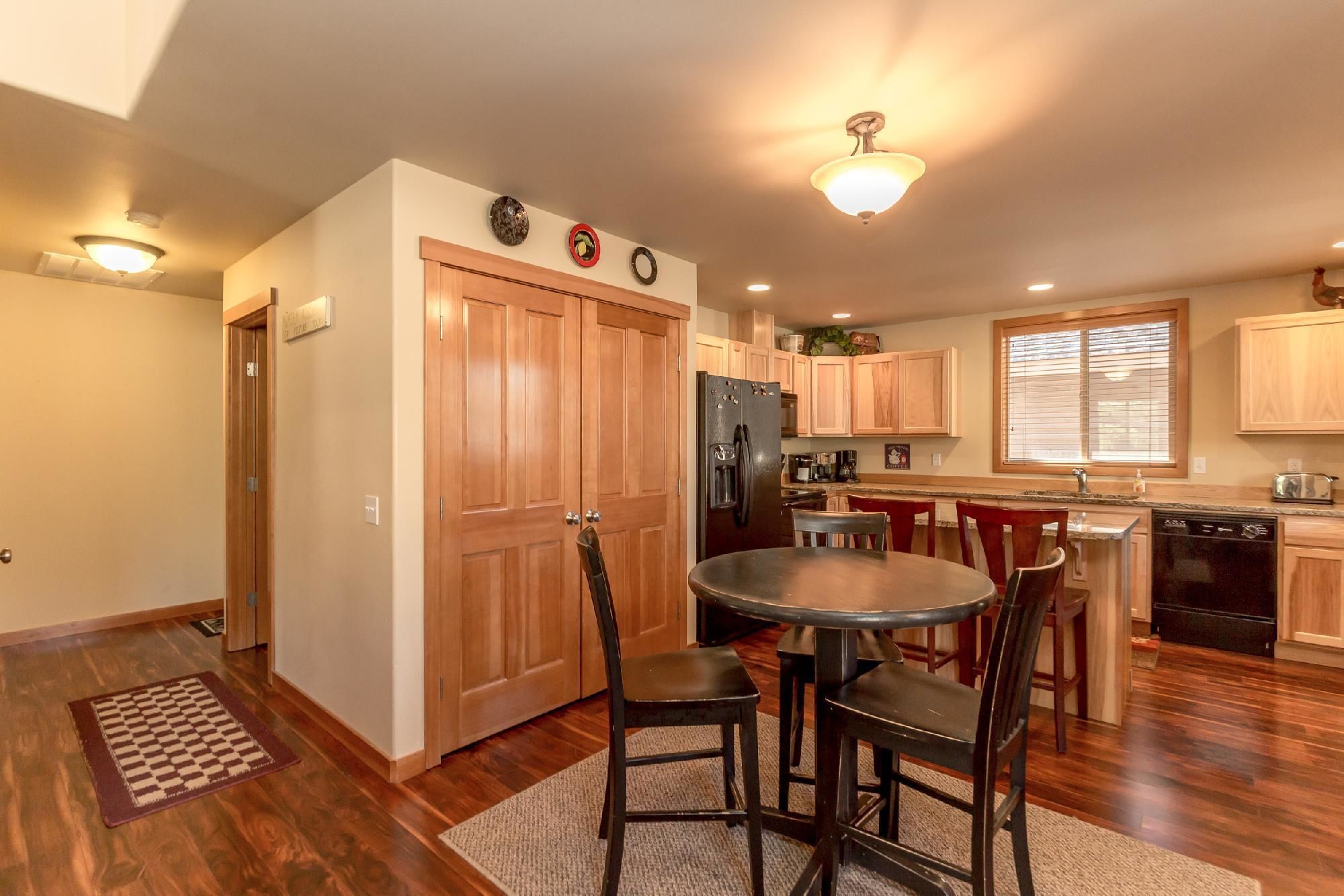 A kitchen with wooden cabinets, a refrigerator, a dining table with chairs, and a window with blinds.