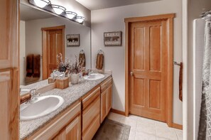 A bathroom with a double sink vanity, wooden cabinets, a large mirror, and a shower area.
