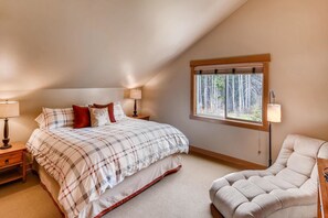 A bedroom with a bed, two bedside tables, a window with a view of trees, and a chair. - Whispering Pines (Cle Elum)
