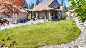 A two-story house with a well-maintained lawn, stone pillars, and a clear view of the surrounding trees. - Whispering Pines (Cle Elum)