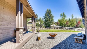 A wooden deck with a fire pit, seating area, and a view of a landscaped garden with trees and a stone wall. - Whispering Pines (Cle Elum)