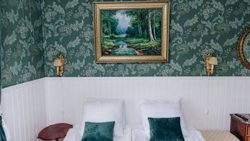 A bedroom with a bed, two pillows, a nightstand, a lamp, and a framed painting of a forest scene.