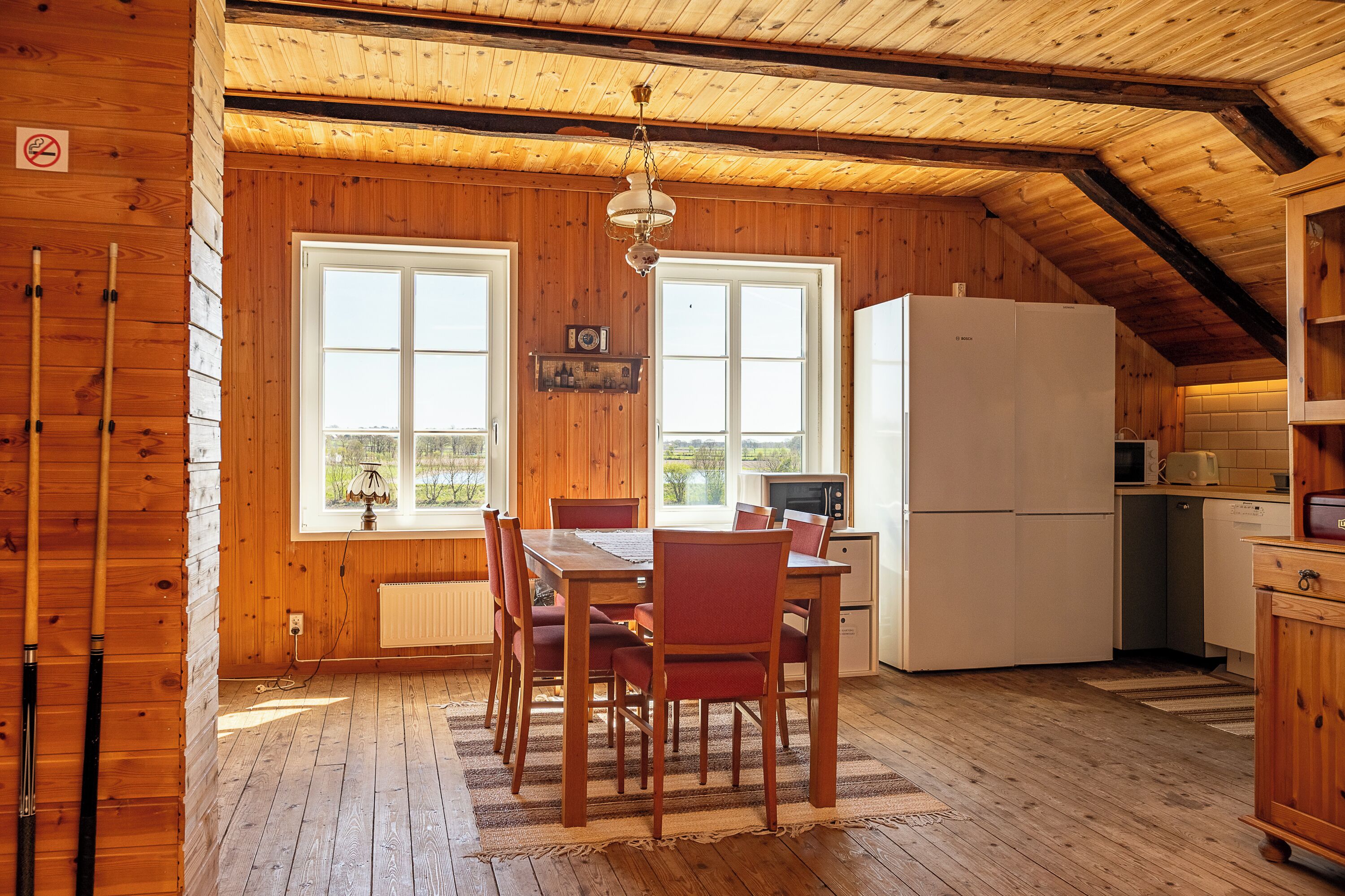 Een houten interieur met een eettafel, stoelen, een koelkast en een keukenhoek.