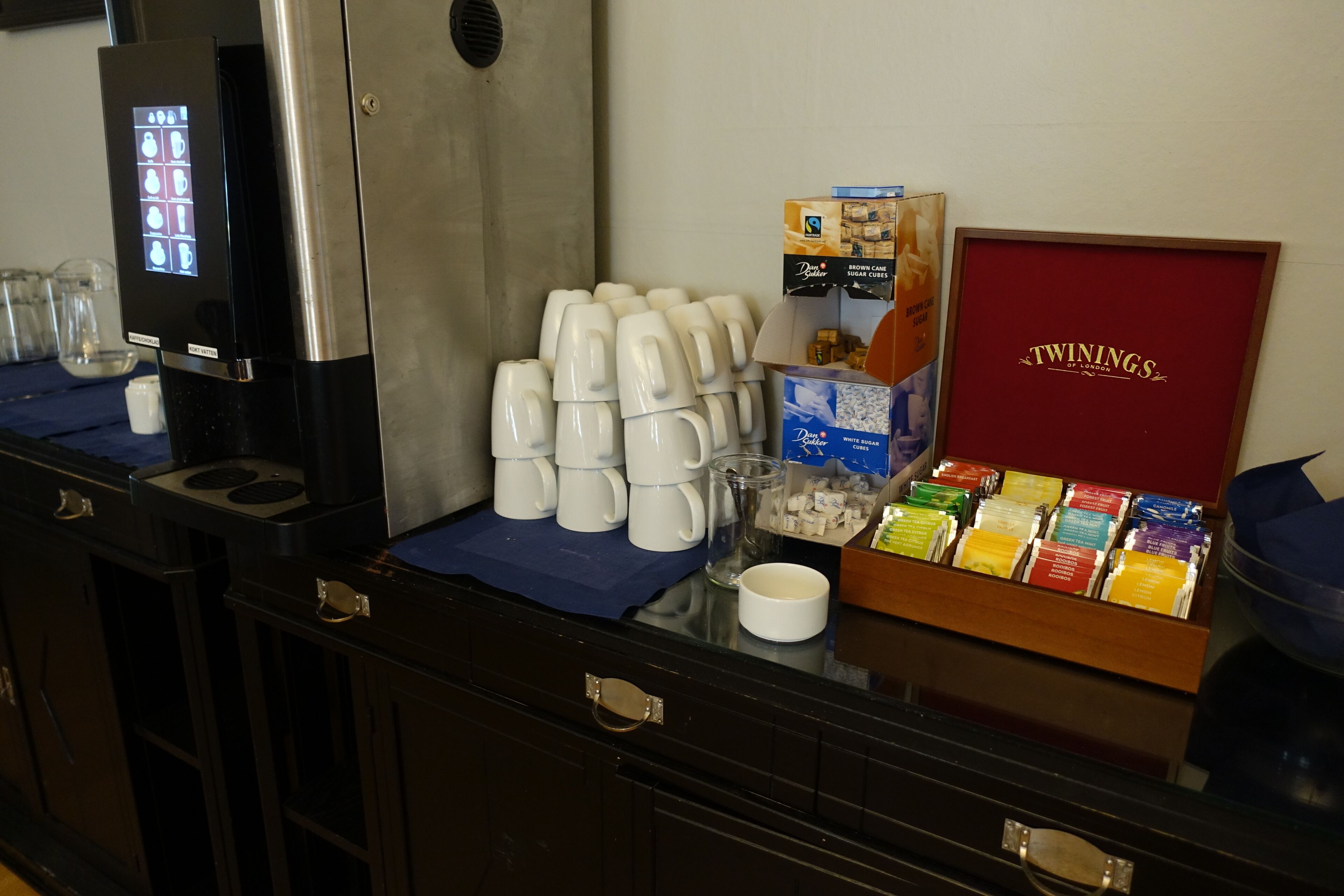 A buffet setup with coffee makers, cups, and Twinings tea boxes.