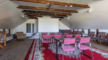 A spacious room with a high ceiling, wooden beams, a red carpet, and rows of pink chairs arranged for seating.