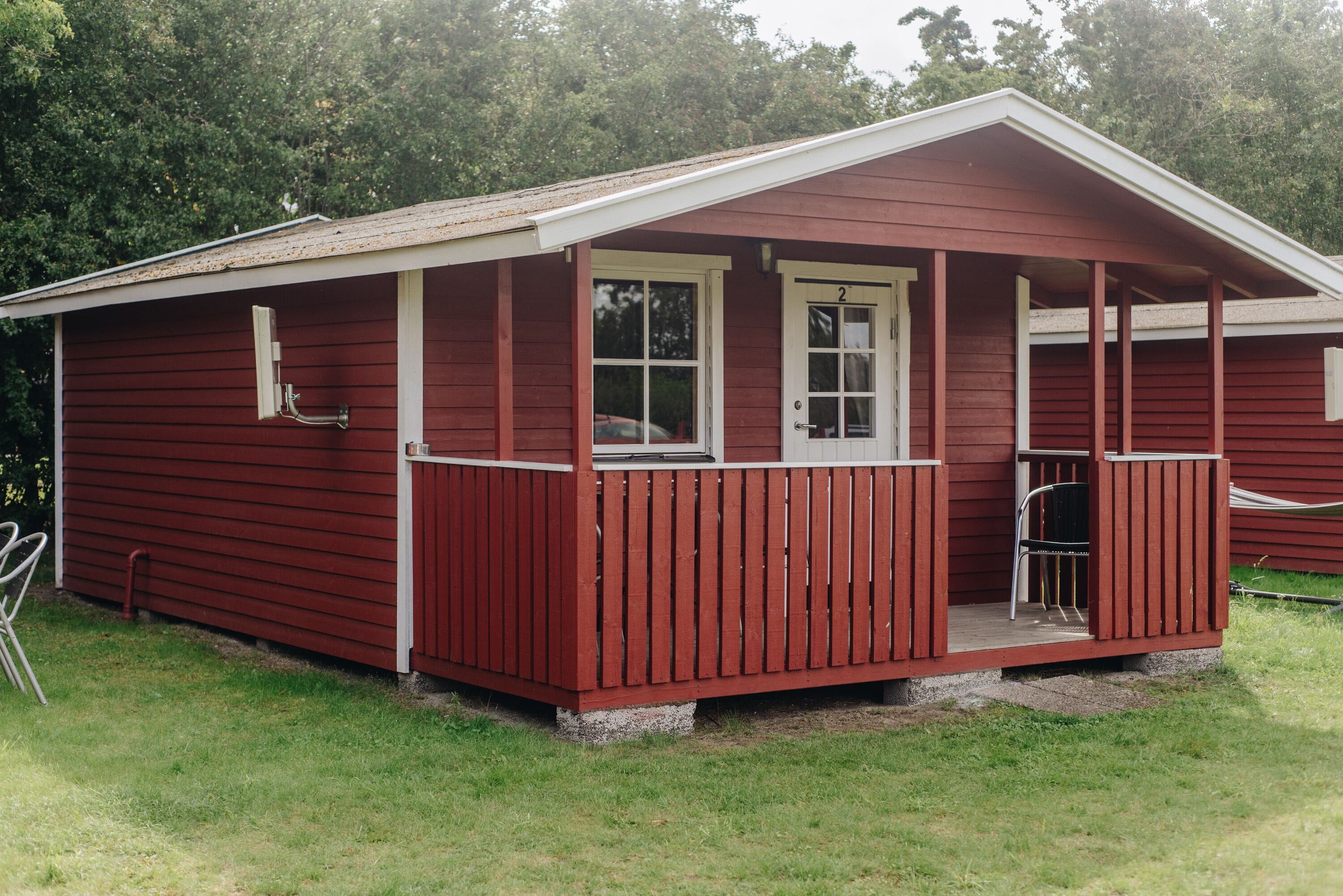 A red wooden cabin with a porch, a door, and a window.