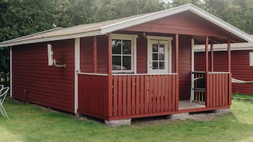 A red wooden cabin with a porch, a door, and a window.
