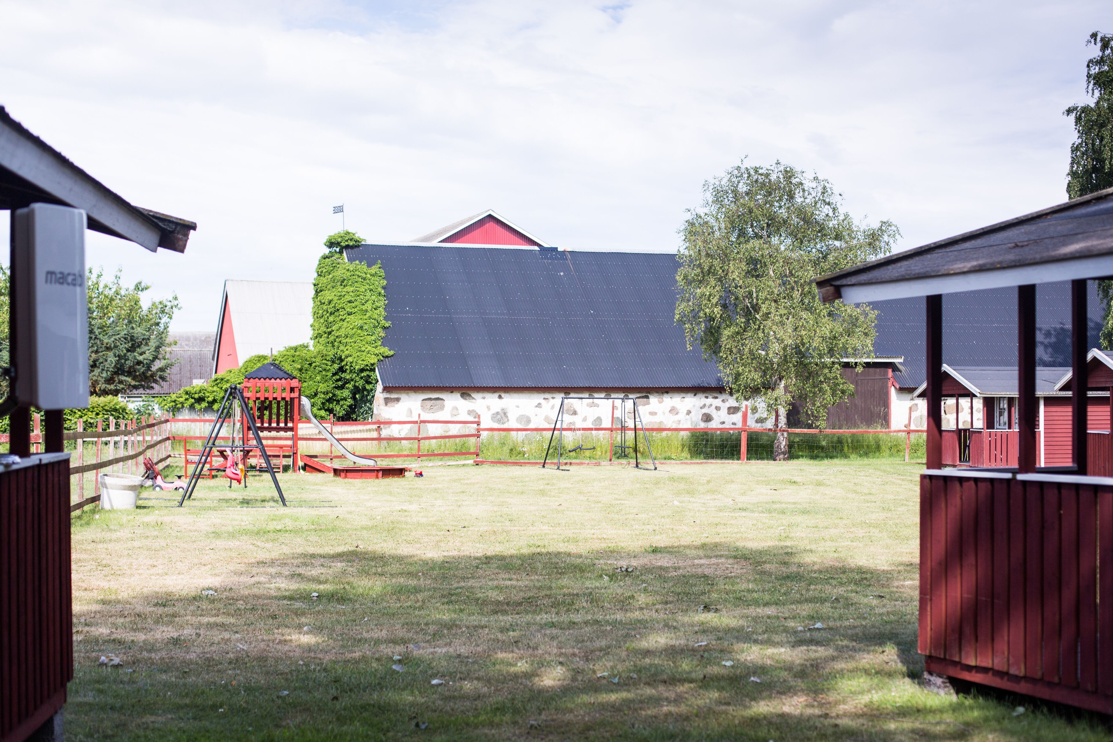 A playground with swings and a slide, surrounded by a fenced area with a stone building in the background.