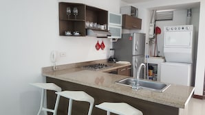 A modern kitchen with a granite countertop, stainless steel appliances, and a bar area with stools. - Apartamento Mistral Cielo Mar (Cartagena)