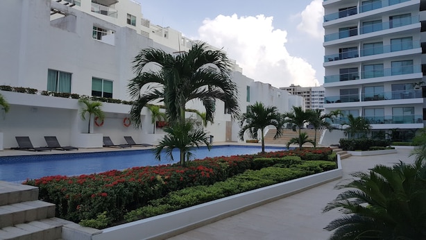 A modern hotel with a swimming pool surrounded by palm trees and red flowers. - Apartamento Mistral Cielo Mar (Cartagena)