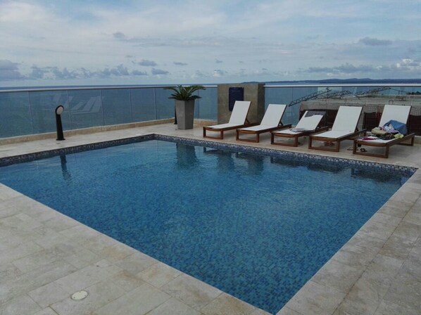 A swimming pool with lounge chairs and a view of the sea.