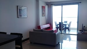 A modern living room with a sofa, a dining table, and a large sliding glass door leading to an outdoor area. - Apartamentos vista mar Milano (Cartagena)