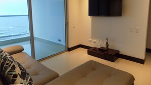 A modern living room with a sofa, a flat-screen TV mounted on the wall, and a view of the ocean through a sliding glass door. - Apartamentos vista mar Milano (Cartagena)