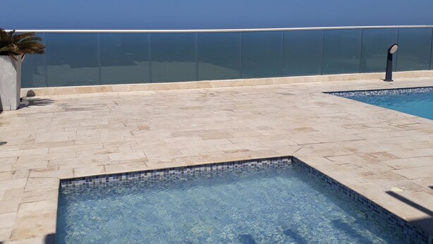 A clear blue sky, a swimming pool with tiled edges, and a glass balustrade. - Apartamentos vista mar Milano (Cartagena)