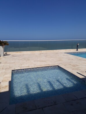 A clear blue sky, a swimming pool with tiled edges, and a glass balustrade.