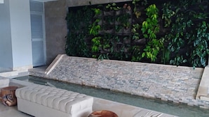 A modern living room with a stone wall, a built-in water feature, and a seating area with a cushioned sofa and ottoman. - Apartamentos vista mar Milano (Cartagena)