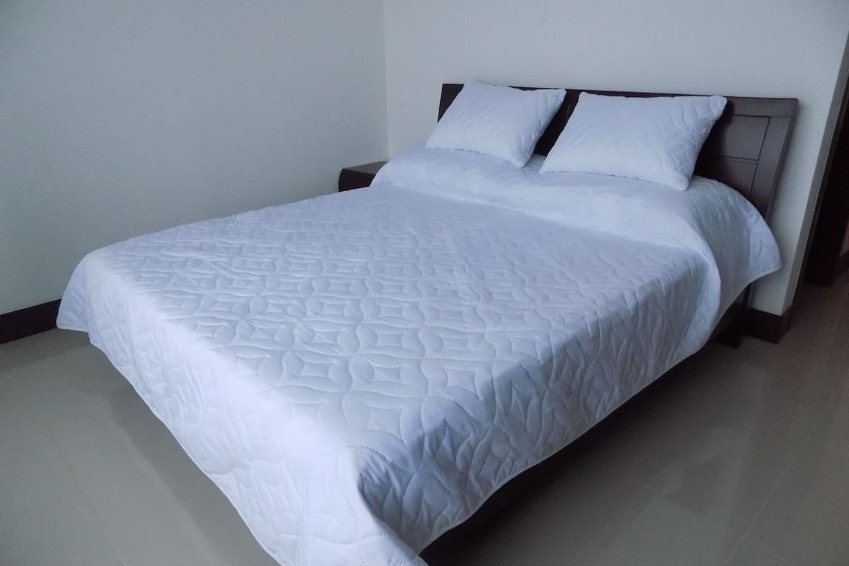 Ein ordentlich bezogenes Bett mit einer gesteppten weißen Tagesdecke und zwei Kissen.