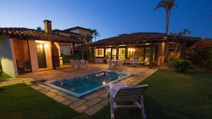A well-lit outdoor pool area with lounge chairs, a patio with tables, and a covered seating area. - Homestay Búzios (Búzios)