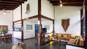 A spacious living area with a wooden ceiling, a television, a sofa, and a dining table with chairs. - Homestay Búzios (Búzios)