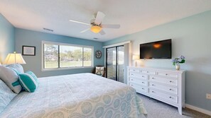 A bedroom with a bed, dresser, TV, and a ceiling fan.