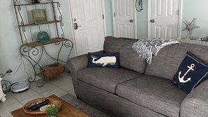 A living room with a grey sofa, a wooden coffee table, and a metal shelf unit. - Quaint Condo Seagrove Beach right fof 30A, quick walk to two beach accessPo (Santa Rosa Beach)