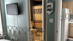 A bedroom with a bed, a TV, a bathroom visible through an open door, and a kitchen area. - Quaint Condo Seagrove Beach right fof 30A, quick walk to two beach accessPo (Santa Rosa Beach)