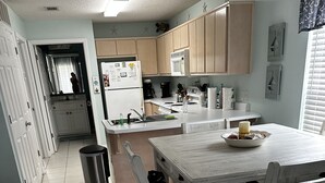 A kitchen with a dining table, chairs, a trash can, and a refrigerator. - Quaint Condo Seagrove Beach right fof 30A, quick walk to two beach accessPo (Santa Rosa Beach)