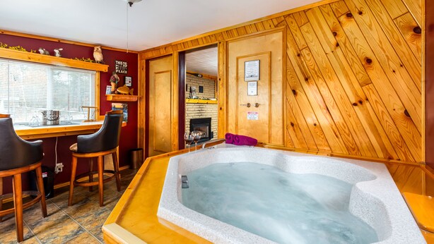 Una habitación con interior de madera, un jacuzzi, zona de cocina con chimenea y barra con taburetes.