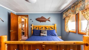 Un dormitorio con cama de madera, decoración de pez en la pared y ventana con cortinas estampadas.