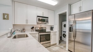 Una cocina moderna con armarios blancos, electrodomésticos de acero inoxidable, encimera de mármol y horno empotrado.
