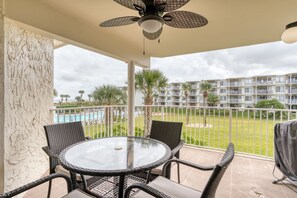 A balcony with wicker furniture, a ceiling fan, and a view of a swimming pool and apartment buildings.