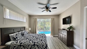 Een slaapkamer met een bed, een plafondventilator, een televisie, een dressoir en uitzicht op een zwembad.