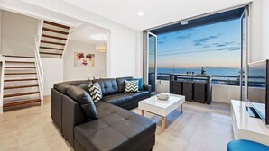 Un salon moderne avec un canapé d’angle noir, une table basse blanche et une grande fenêtre donnant sur la mer.