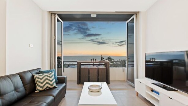 Un salon moderne avec un canapé en cuir, une table basse, un téléviseur à écran plat et un balcon offrant une vue sur la mer.