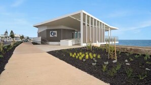 Un bâtiment moderne doté d’un toit plat et de grandes fenêtres, situé près d’une étendue d’eau.