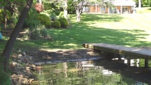 A pond with a wooden dock, surrounded by well-maintained grass and trees. - Here Comes the Sun: 2 Kayaks, Wifi, Ping Pong & Pool table,Sandy Beach, Fenced in Yard, Pet Friendly (Huddleston)