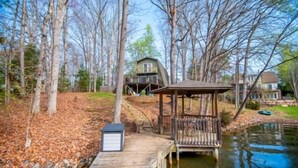 A wooden dock leading to a house with a deck and a gazebo by a lake. - Here Comes the Sun: 2 Kayaks, Wifi, Ping Pong & Pool table,Sandy Beach, Fenced in Yard, Pet Friendly (Huddleston)