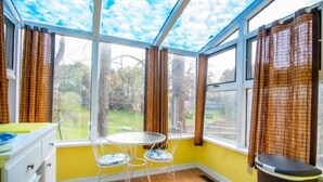A room with a glass ceiling, a dining table with chairs, a trash bin, and a view of greenery outside. - Here Comes the Sun: 2 Kayaks, Wifi, Ping Pong & Pool table,Sandy Beach, Fenced in Yard, Pet Friendly (Huddleston)
