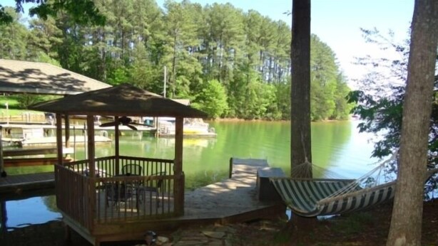 A wooden deck with a gazebo, a hammock, and a view of a lake surrounded by trees. - Here Comes the Sun: 2 Kayaks, Wifi, Ping Pong & Pool table,Sandy Beach, Fenced in Yard, Pet Friendly (Huddleston)