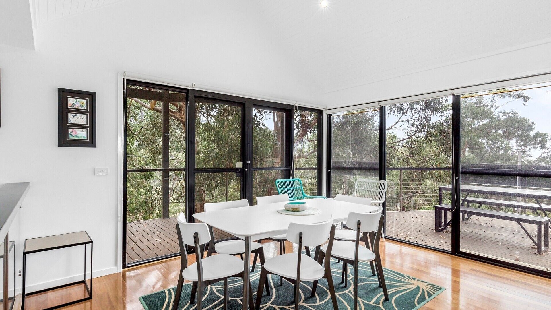 A dining area with a white table and chairs, large windows, and a view of the outdoors.