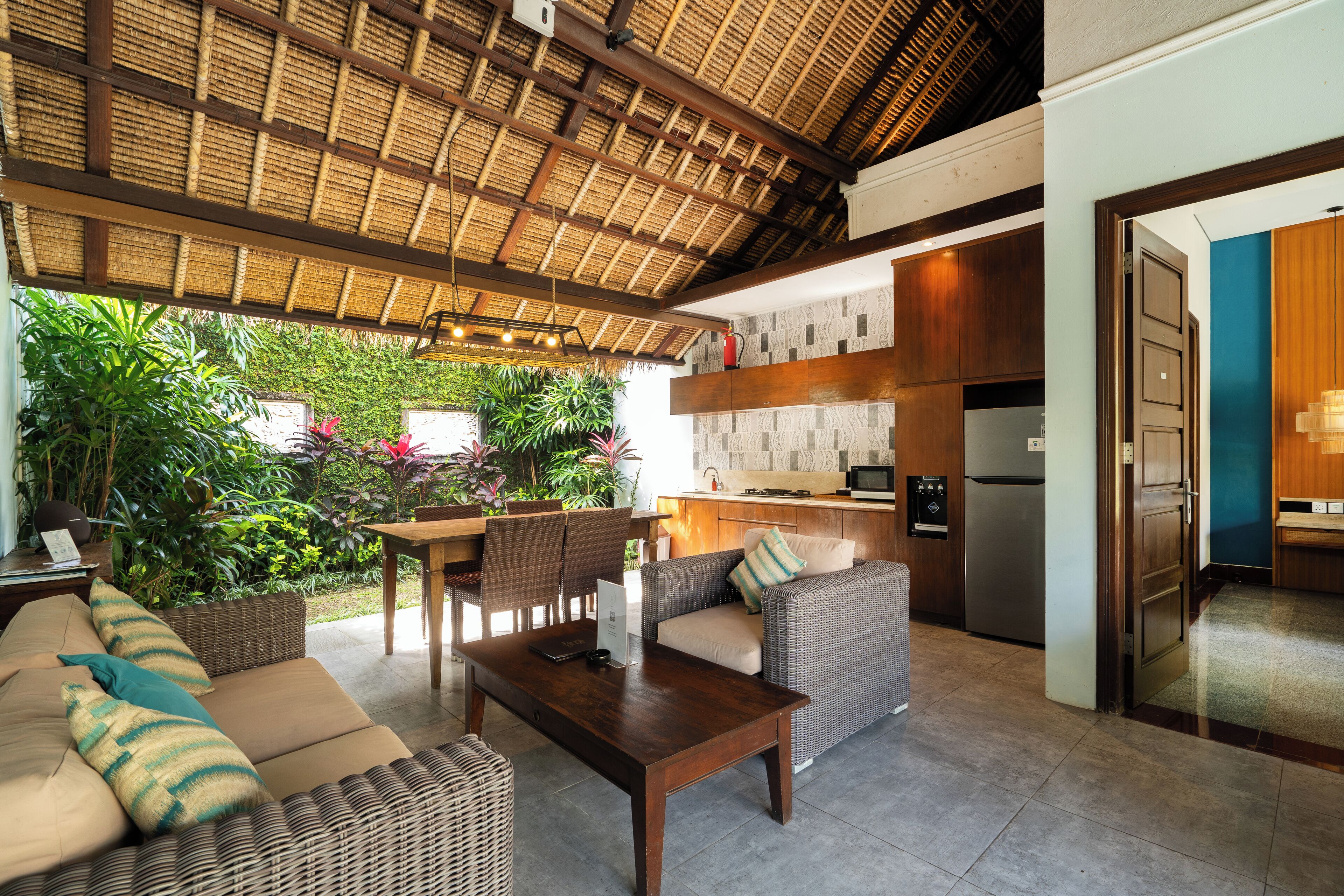 An open-plan living area with a kitchen, a dining set, and a seating area with a thatched roof.
