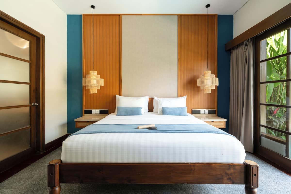 A neatly made bed with a wooden headboard, two bedside tables with lamps, and a large window with curtains.