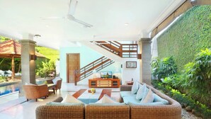 A modern living area with a wicker sofa, a coffee table, and a pool in the background. - Kecapi Villa Seminyak (Seminyak)