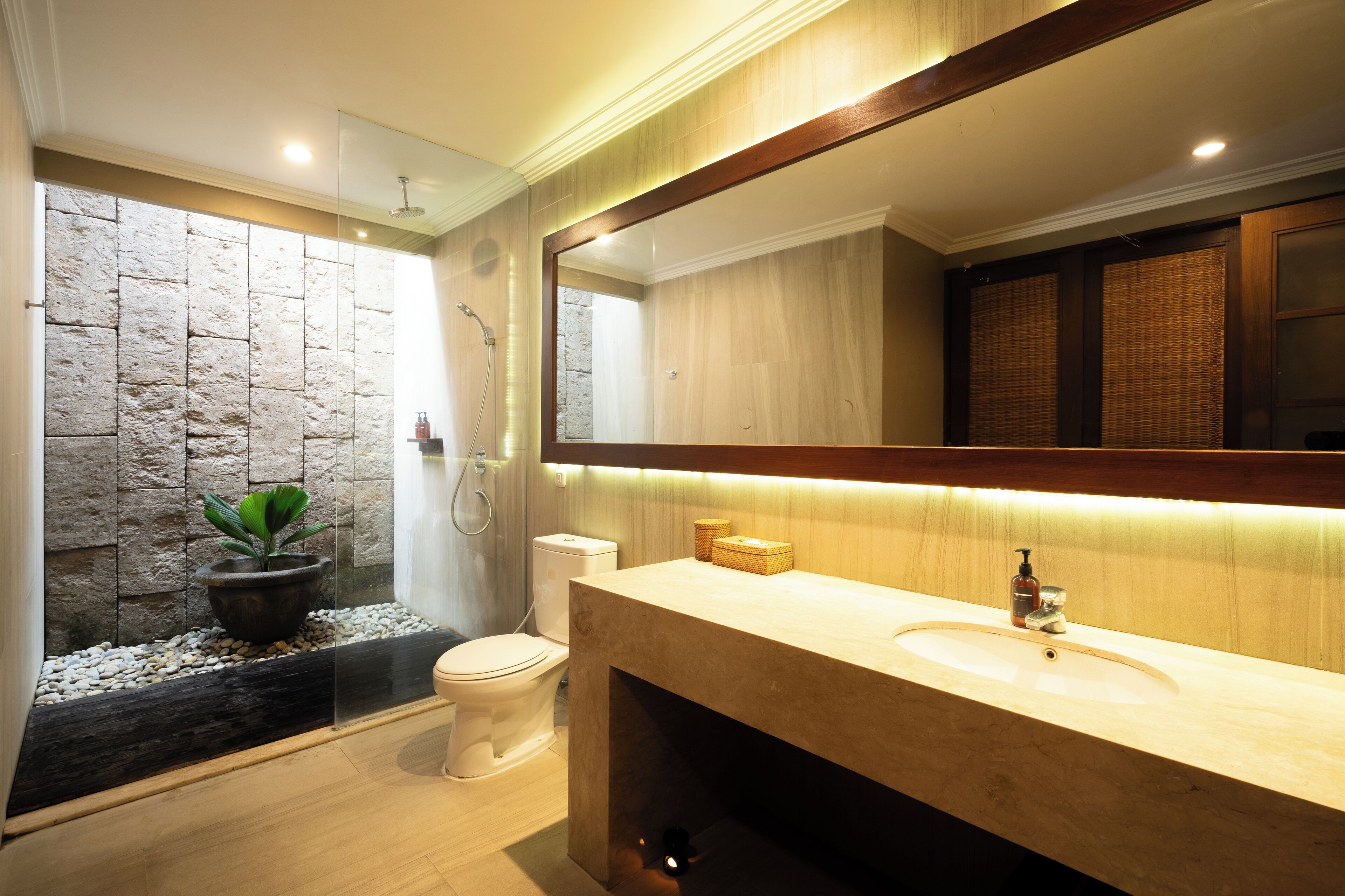 A modern bathroom with a stone accent wall, a large mirror, a sink, and a shower.